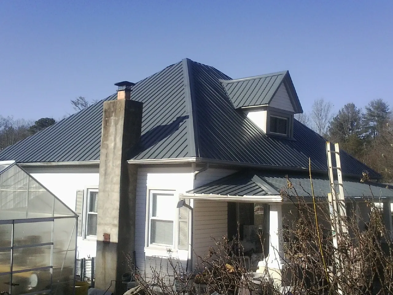 Dark blue standing seam metal roof on a white farmhouse with dormer — Slate & Tile Roof Repair by Roofing Brothers in North Bay