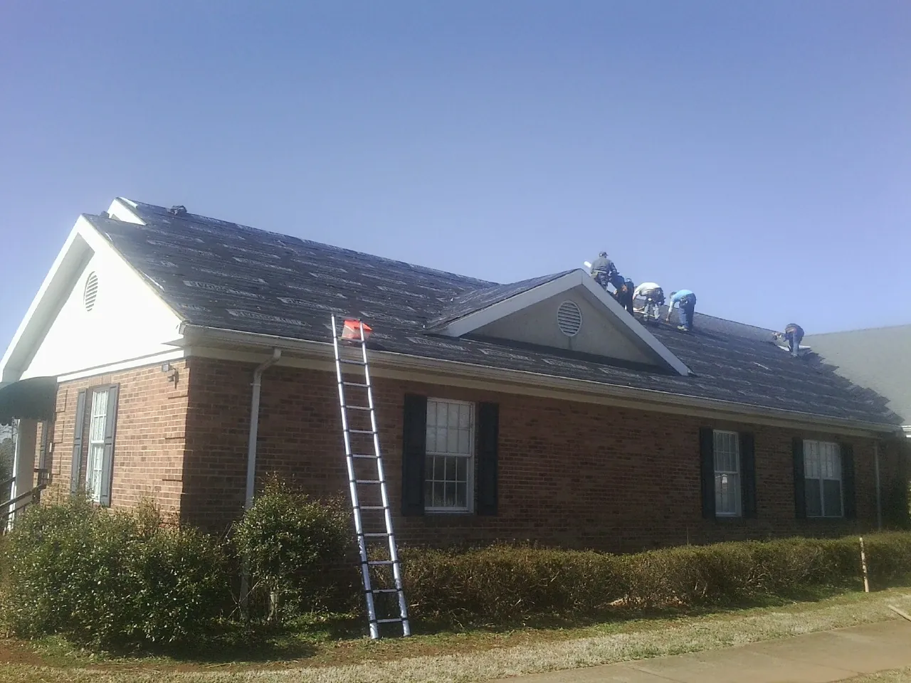 Crew tearing shingles off a brick ranch roof with a ladder set — Emergency Roof Repair work by our crew in North Bay