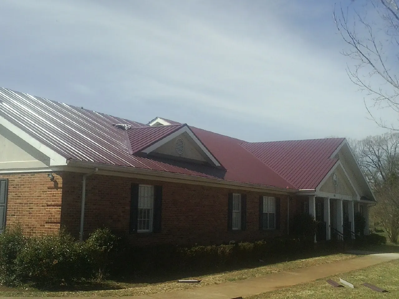 Red metal roof with gabled entries on a long brick building, from a Hail Damage Roof Repair job in North Bay