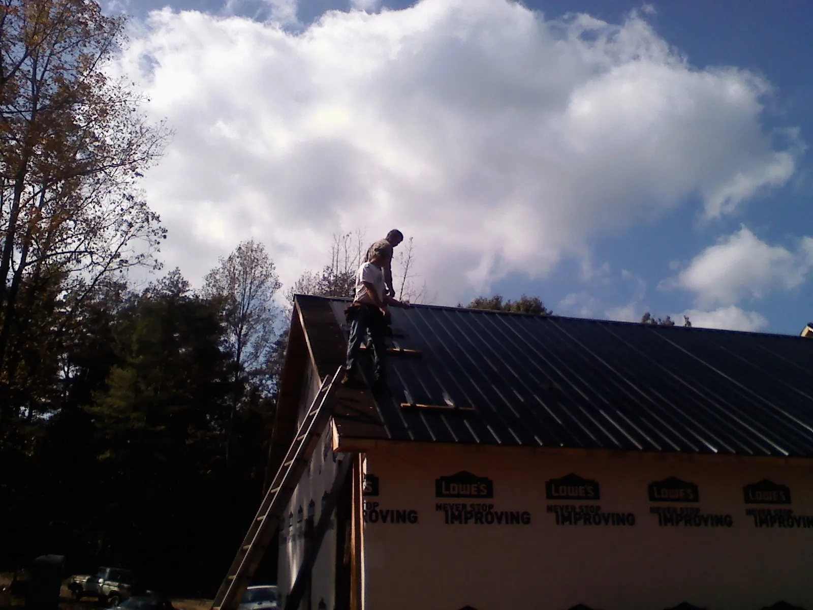Roofer fastening dark metal panels high against a cloudy sky, from a Roof Inspection job in North Bay