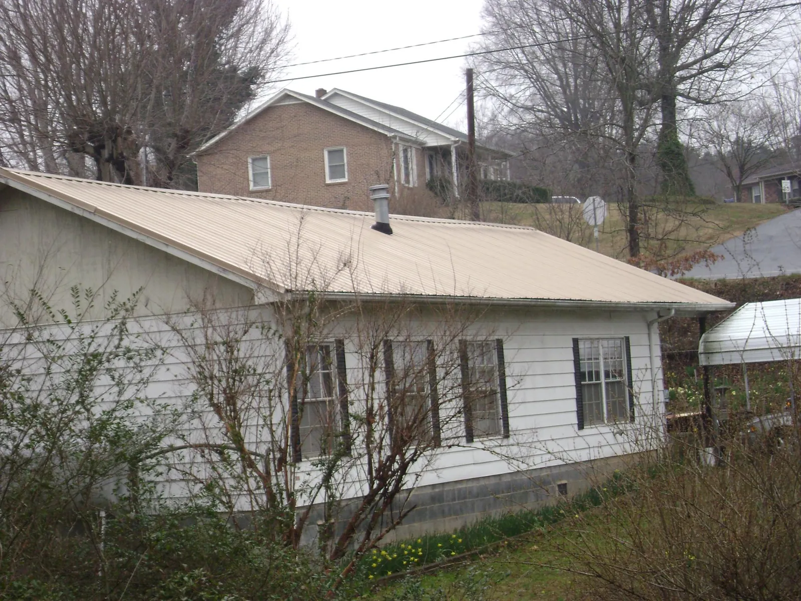 Tan metal roof on a white sided house set into a hillside — Commercial Roofing by Roofing Brothers in North Bay