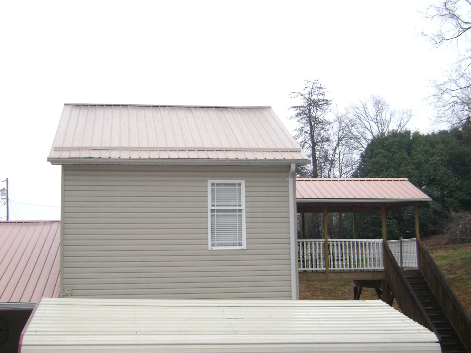 Tan metal roofs on a two story addition and attached porch, from a Roof Replacement job in North Bay